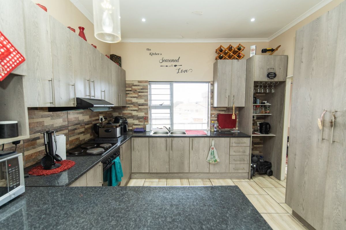 A functional kitchen featuring light wood-grain cabinetry, dark stone-look countertops, a built-in electric hob with extractor, and a double stainless steel sink.