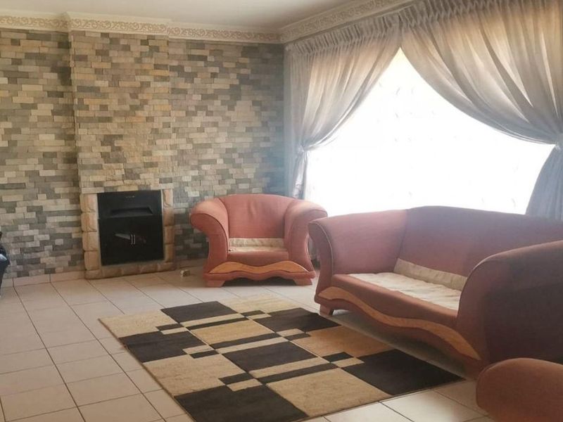 A living room featuring a prominent stone-clad fireplace, tiled flooring, and crown molding, offering a cozy and traditional atmosphere.