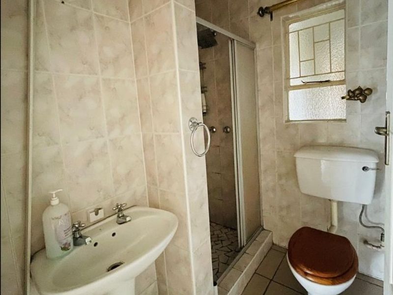 A functional bathroom featuring a pedestal basin, a shower enclosure, and a toilet, finished with neutral wall and floor tiling.