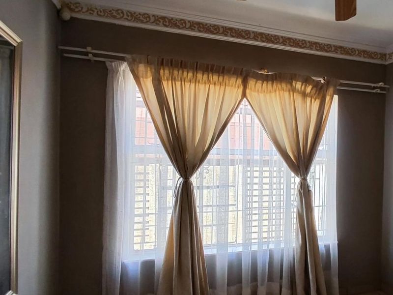A bedroom interior featuring decorative ceiling cornicing and a window fitted with security burglar bars.