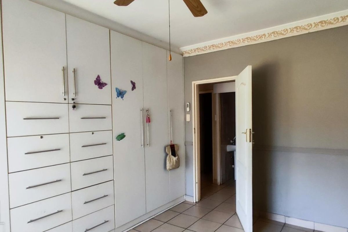 A bedroom featuring extensive built-in cabinetry, tiled flooring, and a ceiling fan, with a doorway leading to an adjacent space.