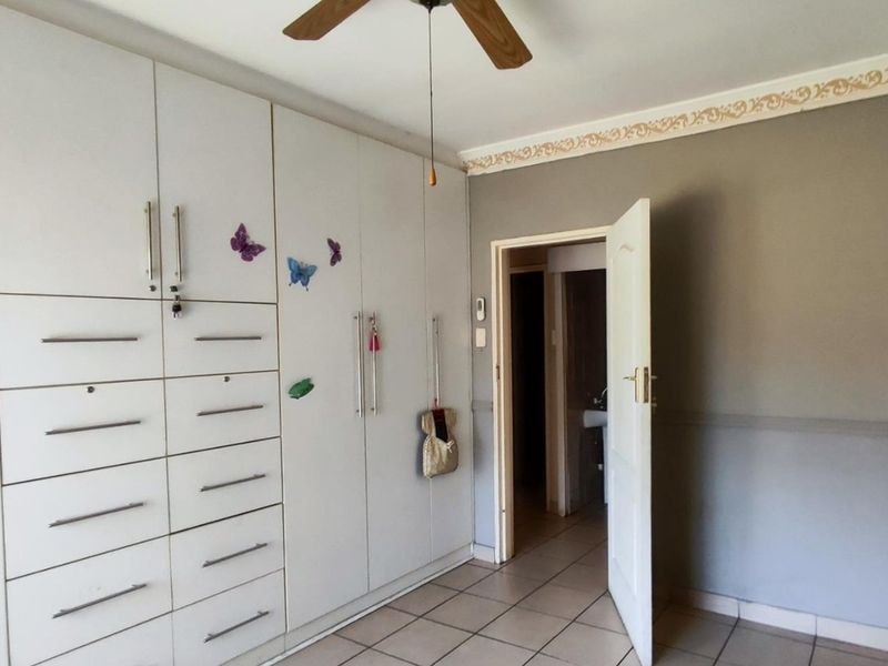 A bedroom featuring extensive built-in cabinetry, tiled flooring, and a ceiling fan, with a doorway leading to an adjacent space.