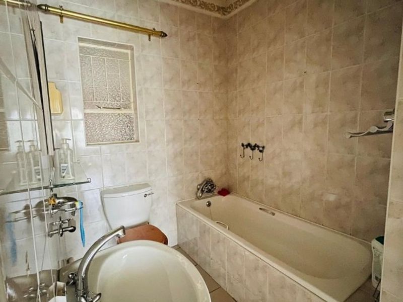 A dated bathroom featuring a bathtub, pedestal basin, and toilet with neutral wall and floor tiling.