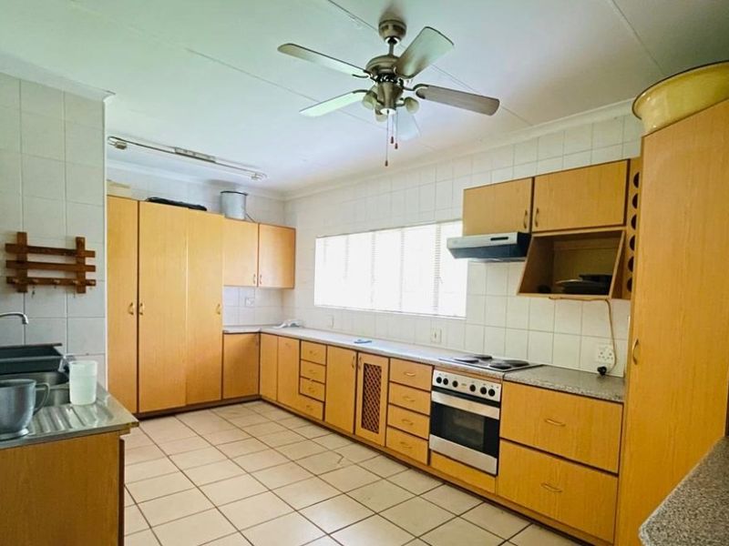 A functional kitchen featuring light wood-tone cabinetry, tiled flooring, built-in oven and hob, and ample storage space, ready for a modern update.