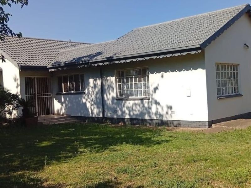 Rear view of a single-story house featuring a tiled roof, steel-framed windows, and a security gate entrance, set within a garden area.
