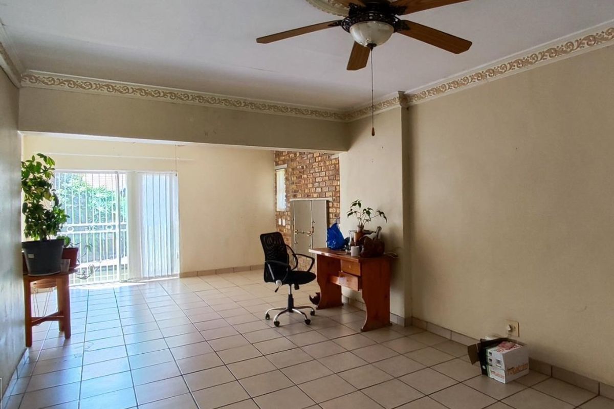 Spacious living area featuring tiled flooring, a ceiling fan, decorative cornicing, and an exposed brick feature wall with a built-in fireplace.
