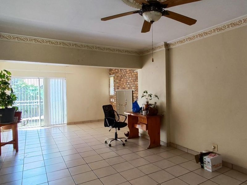 Spacious living area featuring tiled flooring, a ceiling fan, decorative cornicing, and an exposed brick feature wall with a built-in fireplace.
