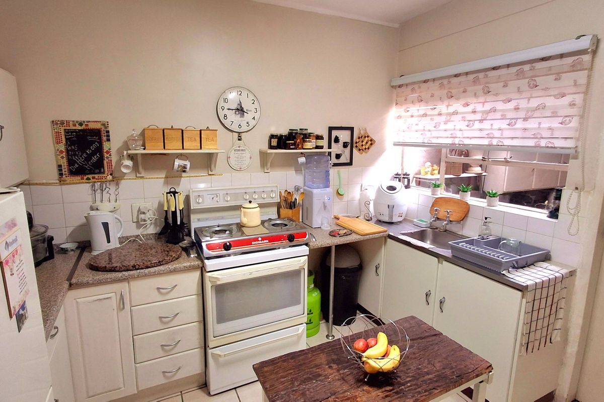 A functional kitchen featuring a freestanding stove, stainless steel sink, tiled backsplash, and ample built-in cabinetry with laminate countertops.