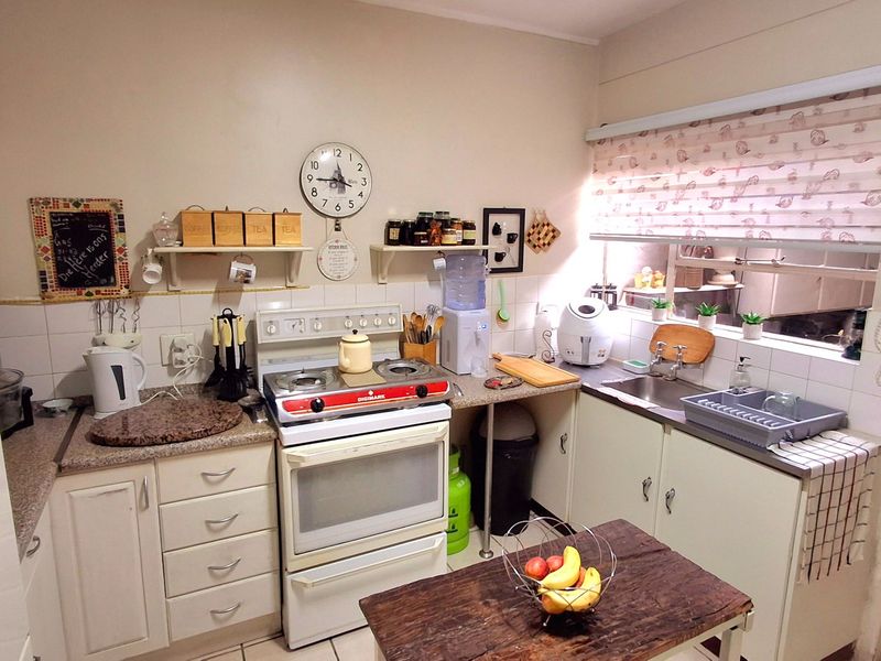 A functional kitchen featuring a freestanding stove, stainless steel sink, tiled backsplash, and ample built-in cabinetry with laminate countertops.