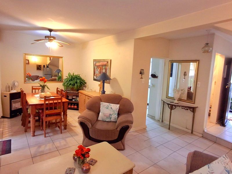 An open-plan living and dining area featuring neutral tiled flooring, a ceiling fan, and direct access to adjacent rooms.