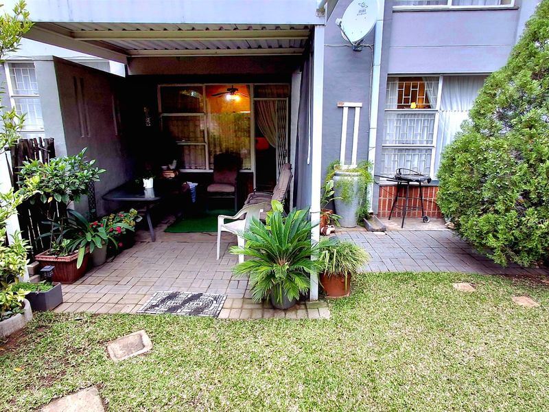 A paved, covered patio area leading into the apartment, featuring a small garden space and exterior security gate.