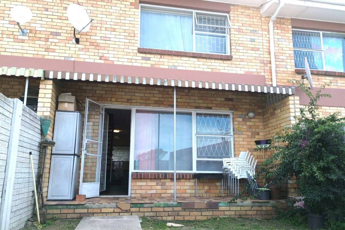 Rear exterior view of a brick apartment featuring a covered patio area, security gates, and window bars.