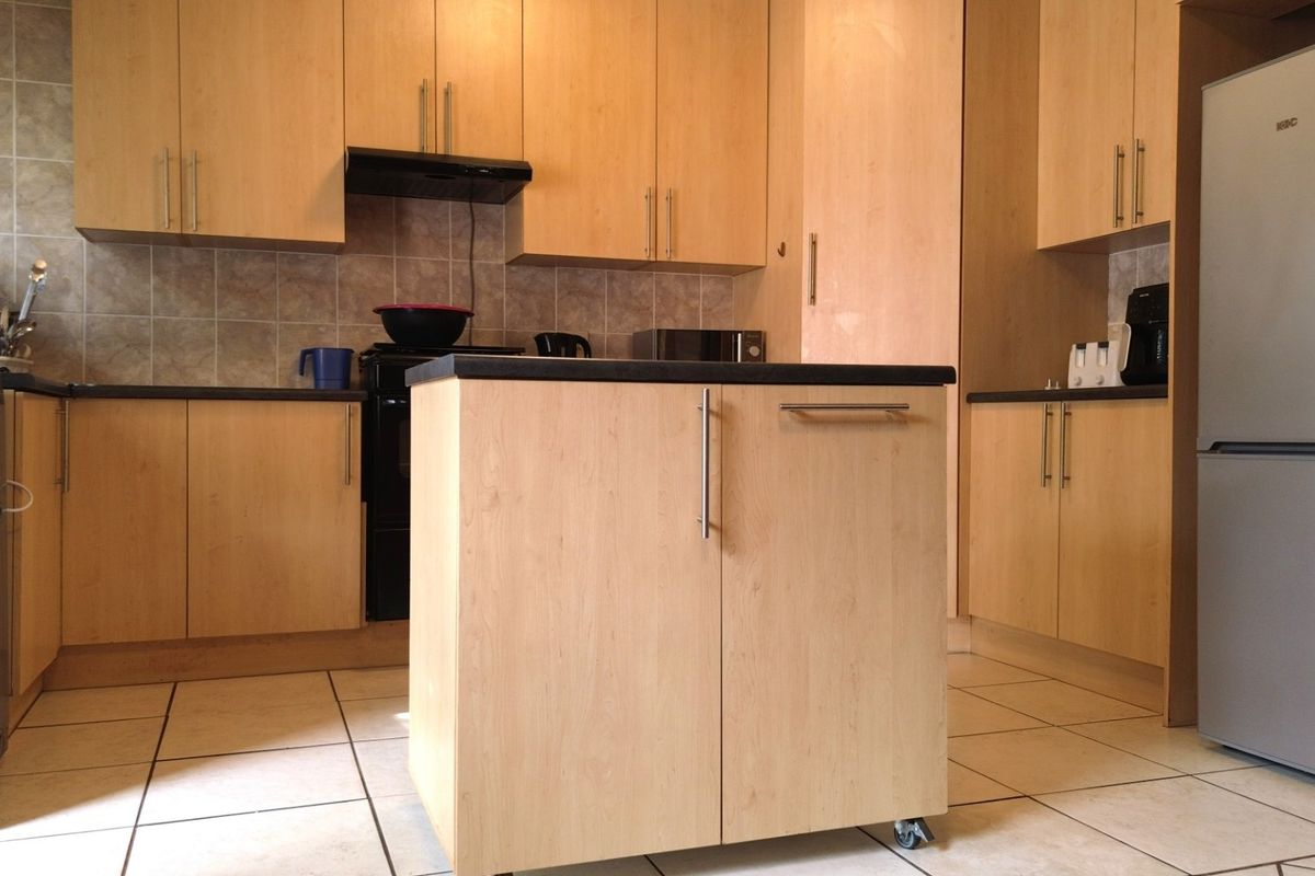 A functional kitchen featuring light wood-finish cabinetry, tiled backsplash, tiled flooring, and a central mobile island unit.