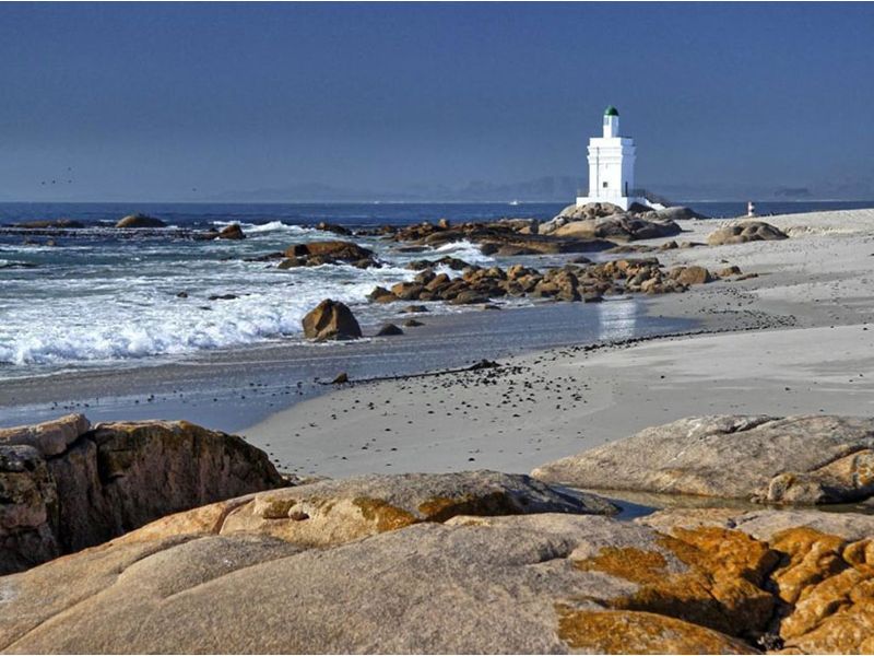 A scenic coastal view featuring a white lighthouse situated on a rocky shoreline overlooking the ocean and sandy beach.