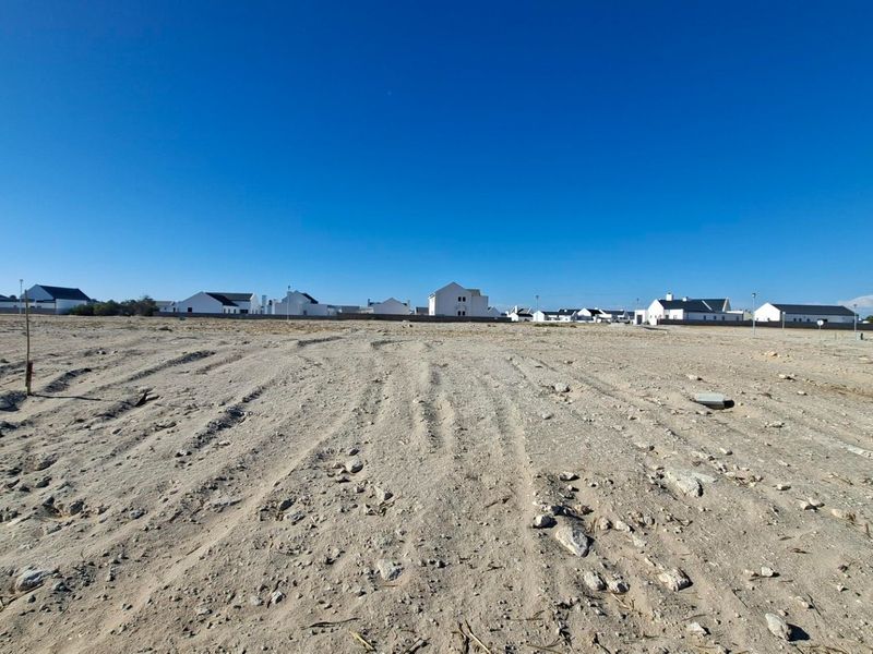 A wide-angle view of a vacant residential plot of land with surrounding neighborhood houses visible in the background.