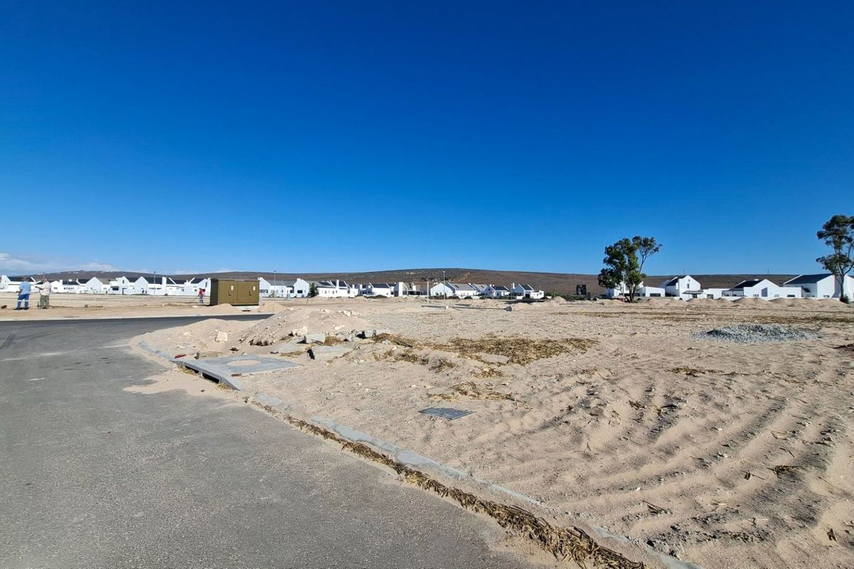 A vacant residential plot featuring an asphalt road frontage, concrete curbing, and an installed utility box, situated in a developing residential estate.