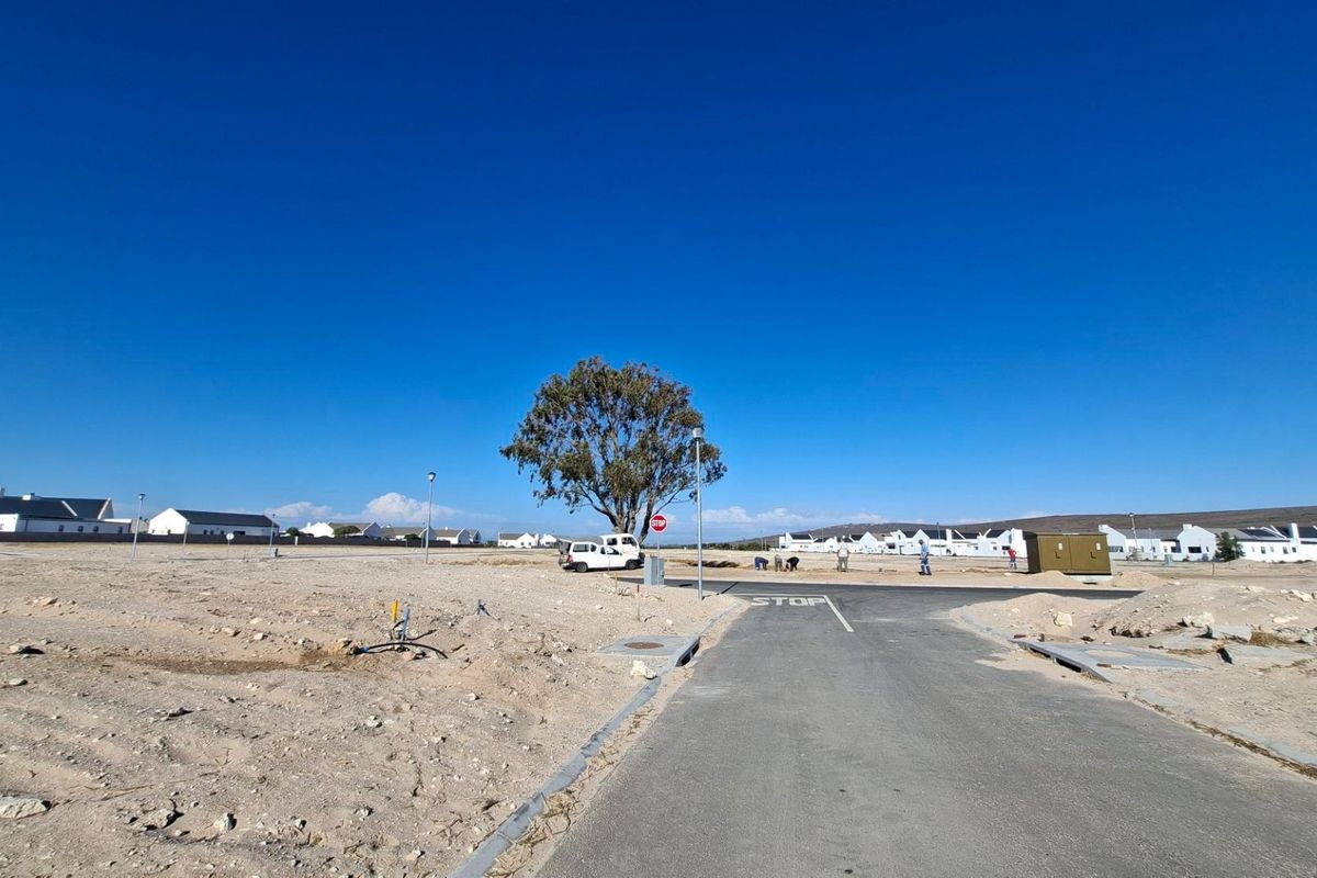 A vacant residential plot featuring a paved access road, established utility connections, and clear views of the surrounding estate development.