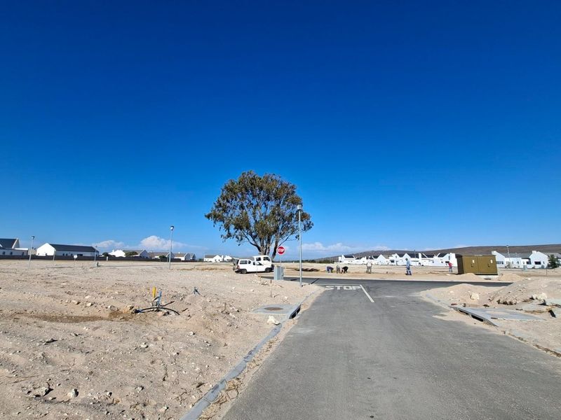 A vacant residential plot featuring a paved access road, established utility connections, and clear views of the surrounding estate development.