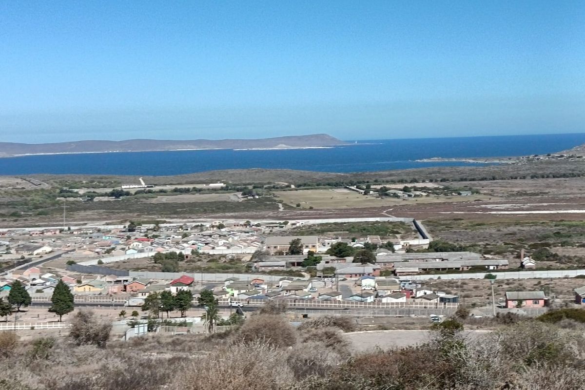 An elevated aerial view overlooking a residential neighborhood with coastal landscape and ocean in the background.