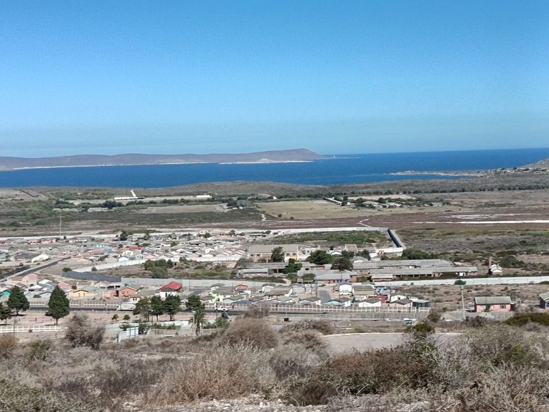 An elevated aerial view overlooking a residential neighborhood with coastal landscape and ocean in the background.