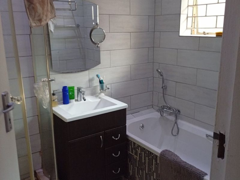 A functional bathroom featuring a vanity unit, shower enclosure, bathtub, and tiled finishes, providing a practical and well-maintained space.