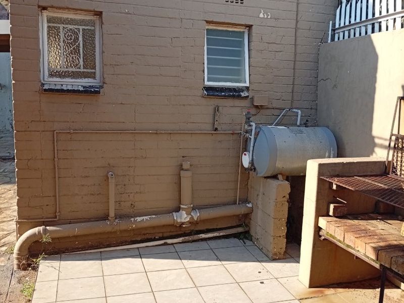 Rear exterior area featuring a tiled patio, built-in braai, and external geyser unit mounted against a painted brick wall.