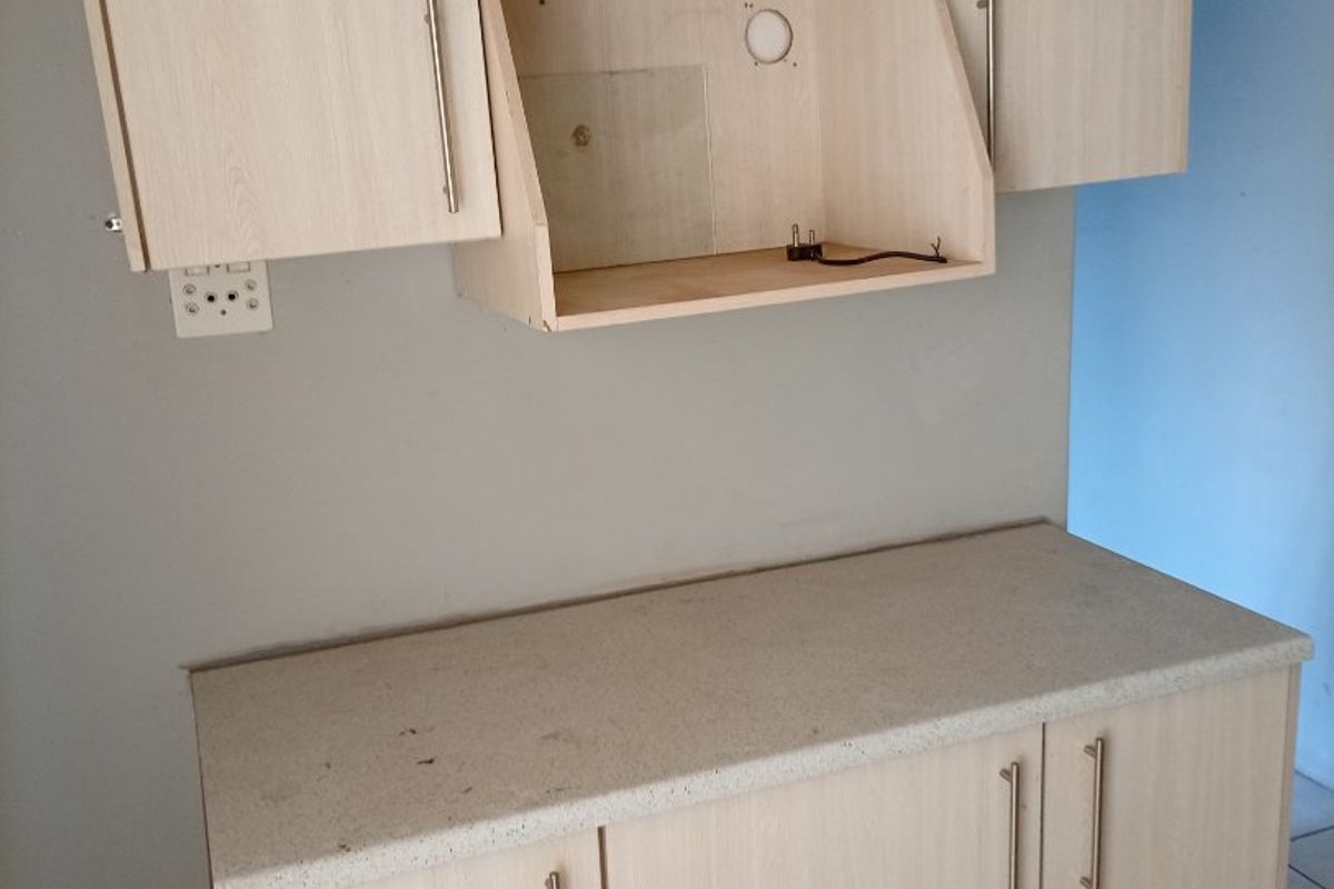 A kitchen prep area featuring light wood-look built-in cabinetry, a laminate countertop, and tiled flooring, currently missing an extractor fan unit.
