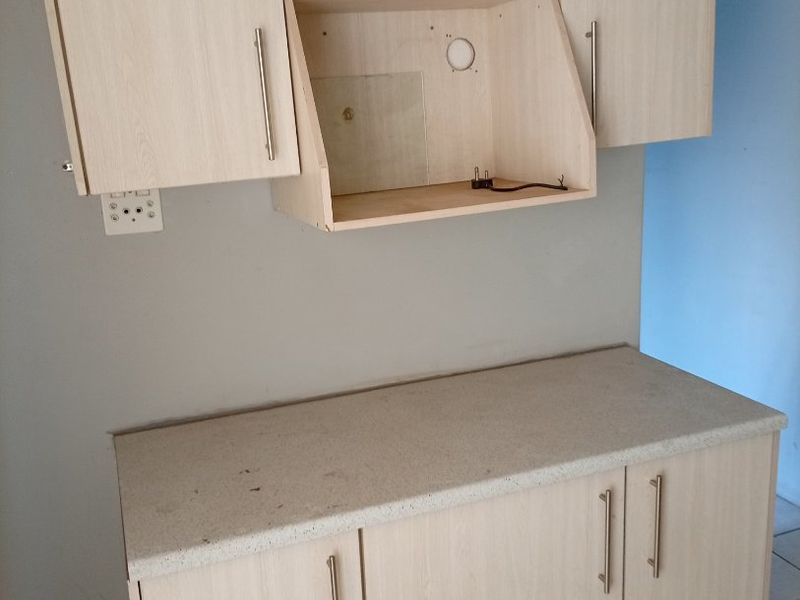 A kitchen prep area featuring light wood-look built-in cabinetry, a laminate countertop, and tiled flooring, currently missing an extractor fan unit.
