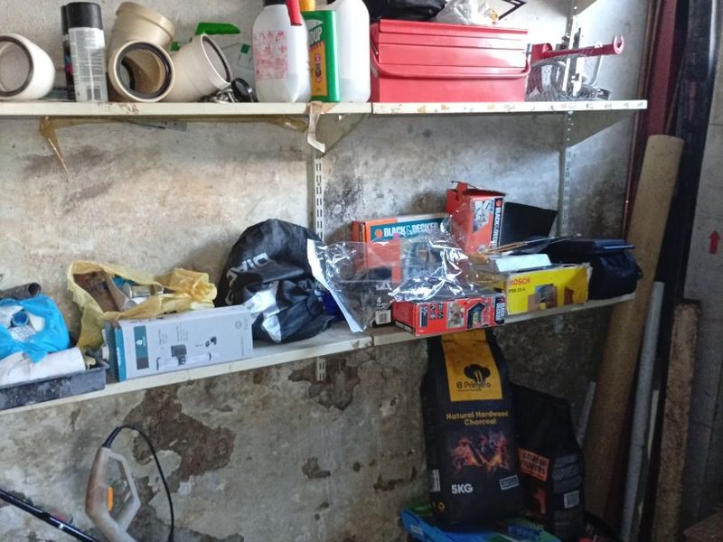 A garage storage area featuring wall-mounted shelving units against a concrete wall showing signs of surface wear and peeling paint.