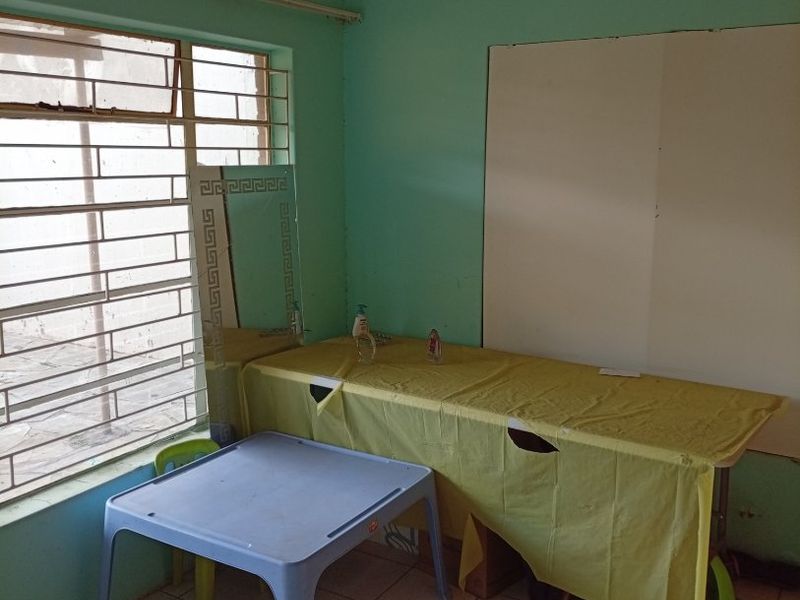 A bedroom featuring tiled flooring, security bars on the window, and ventilation grilles, currently used as a workspace.
