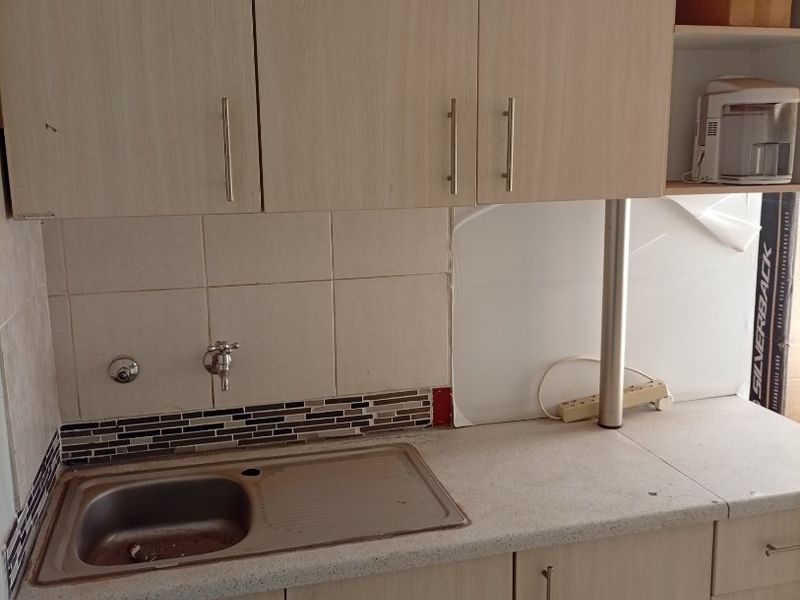 A functional scullery or utility area featuring laminate cabinetry, a stainless steel sink, and tiled splashback, providing practical prep and wash-up space.