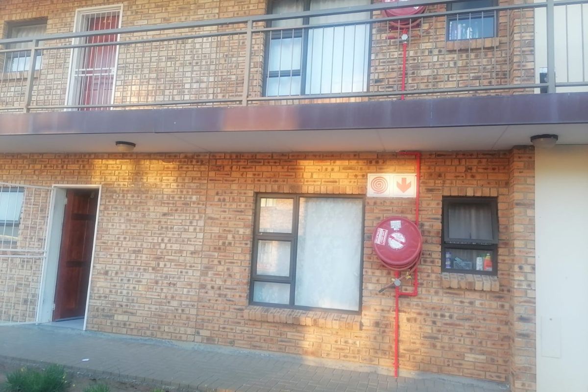 Exterior view of a face brick apartment building featuring metal balcony railings, aluminium window frames, and mounted fire safety equipment.