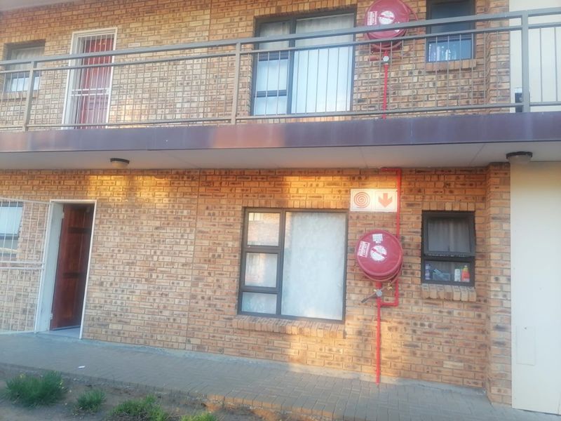 Exterior view of a face brick apartment building featuring metal balcony railings, aluminium window frames, and mounted fire safety equipment.