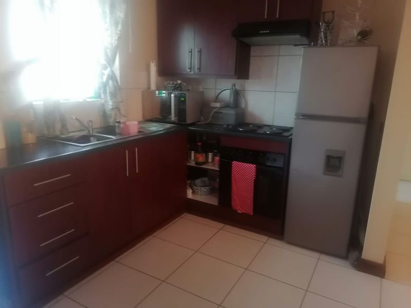 A functional kitchen featuring dark wood cabinetry, tiled backsplash, built-in oven with hob, and tiled flooring.