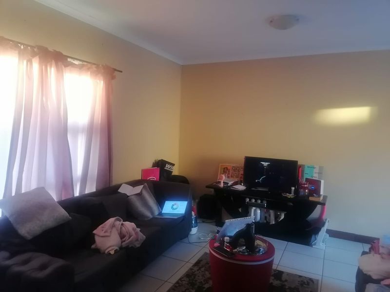 A living room area featuring tiled flooring and a window with a curtain rod, providing a functional space for relaxation.