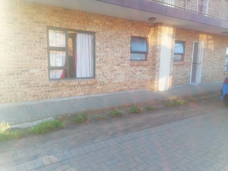 Front exterior view of an apartment building featuring face brick facade, aluminium window frames, and a paved walkway entrance.