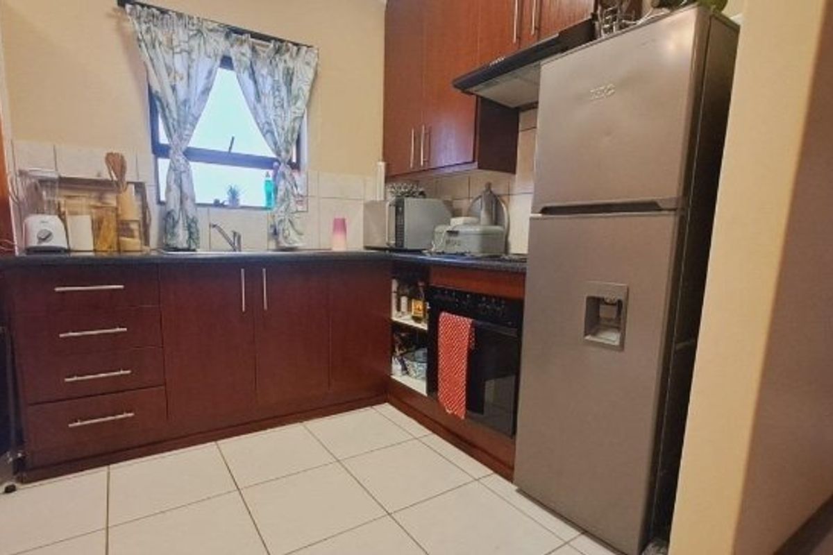 A functional kitchen featuring dark wood cabinetry, tiled flooring, a built-in oven with extractor fan, and a stainless steel sink.