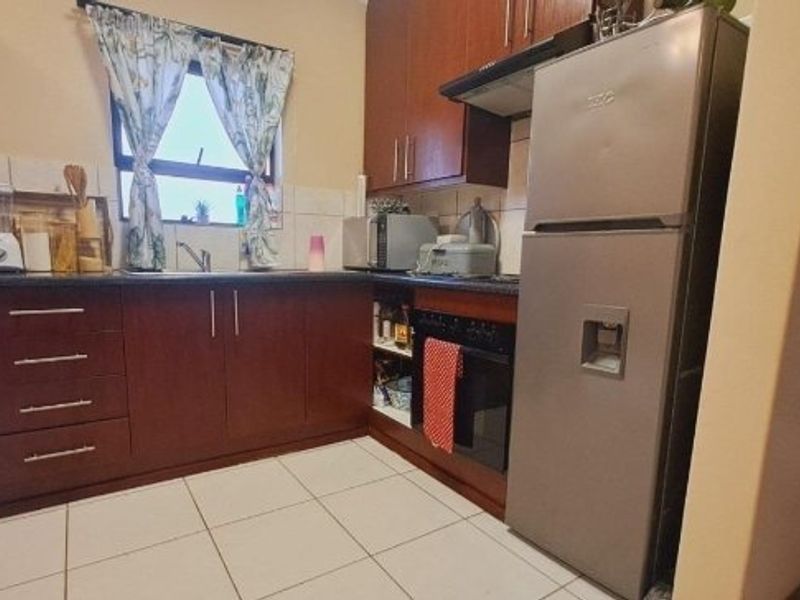 A functional kitchen featuring dark wood cabinetry, tiled flooring, a built-in oven with extractor fan, and a stainless steel sink.