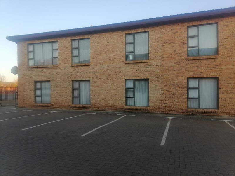 Exterior view of a two-story apartment building featuring face brick construction, aluminium window frames, and an adjacent paved parking area.