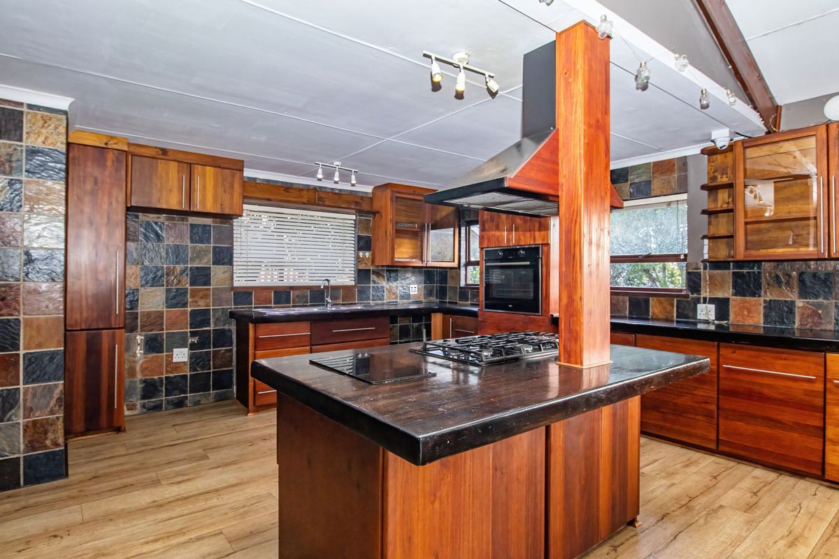 A spacious kitchen featuring wooden cabinetry, a central island with a gas hob, stone tile backsplash, and integrated appliances.