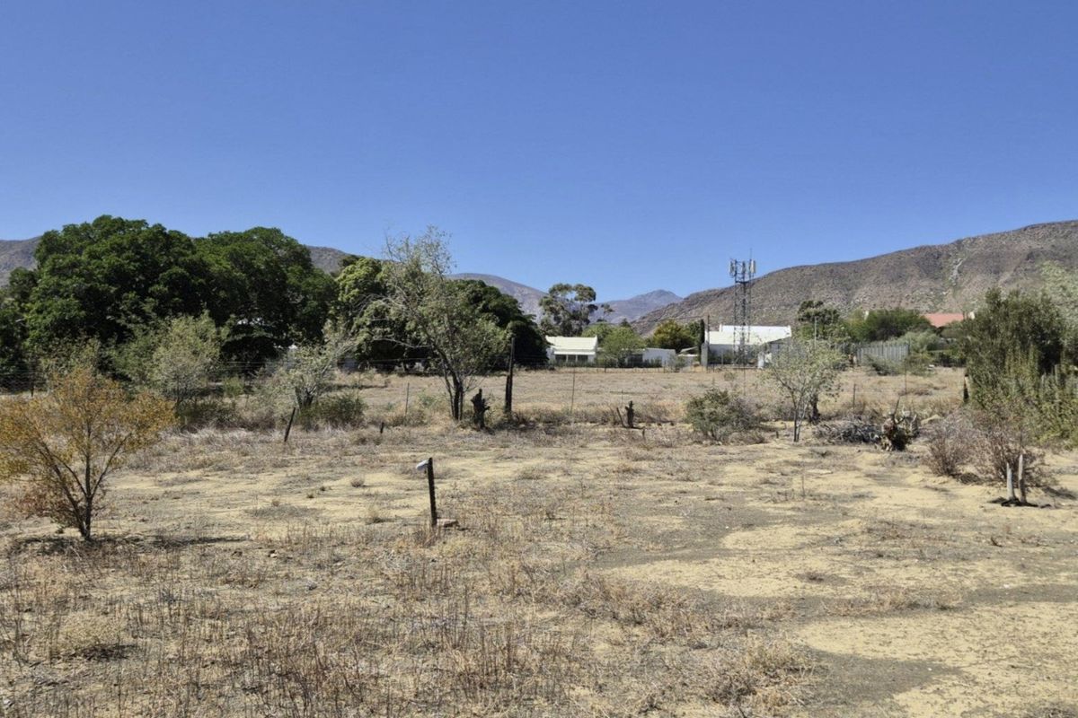 A vacant residential plot featuring dry vegetation, wire fencing, and mountain views in the background.