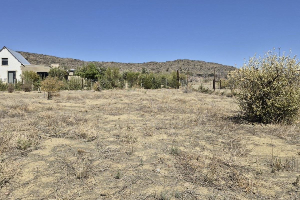 A view of a vacant residential plot featuring dry natural vegetation and perimeter wire fencing with a neighboring structure in the background.