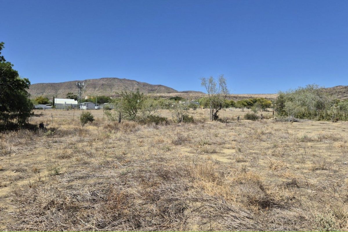 A view of the vacant residential land featuring dry vegetation, wire fencing, and a distant mountain landscape.