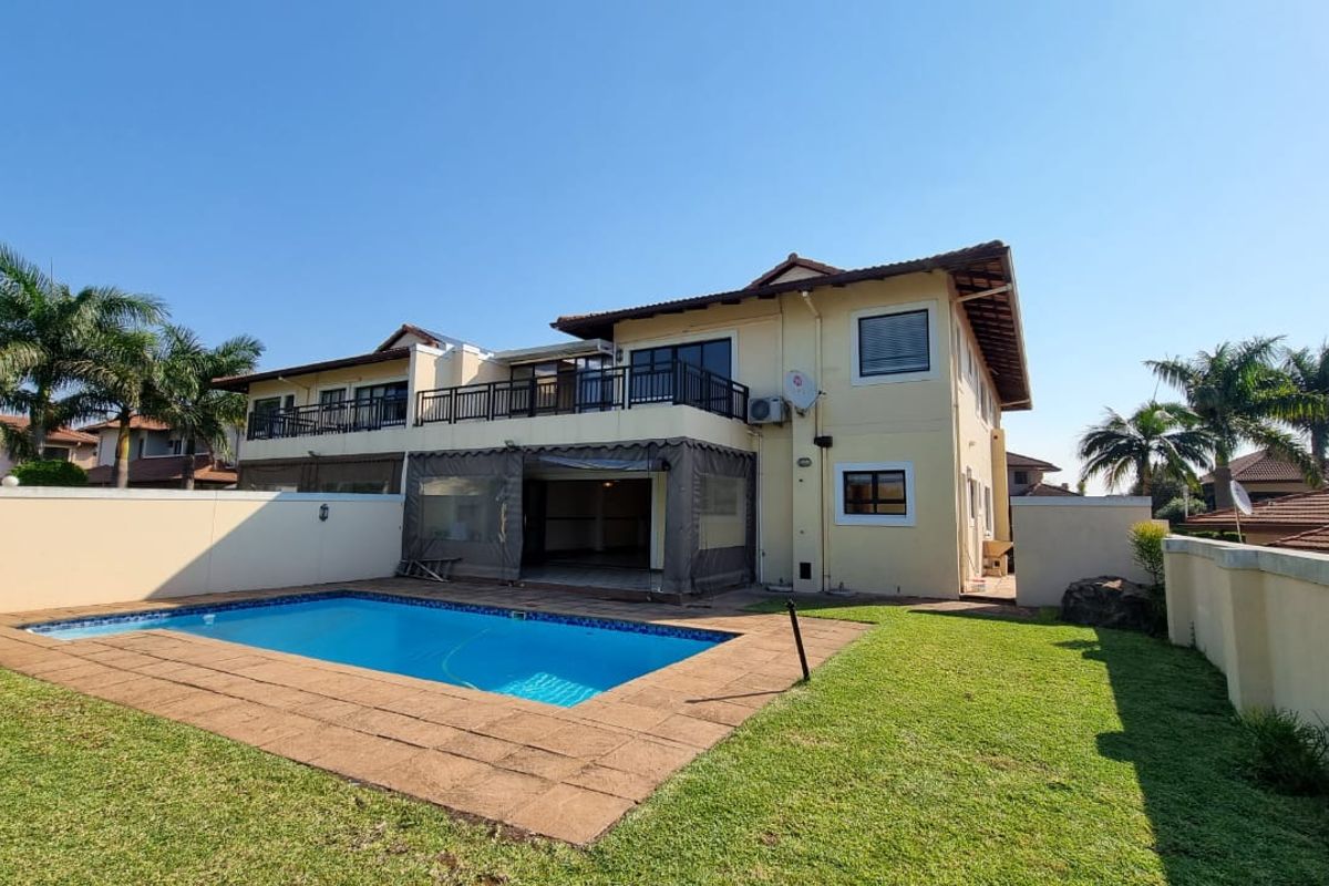 Rear view of the townhouse featuring a private swimming pool, paved deck, lawn area, and an upper-level balcony with metal railings.