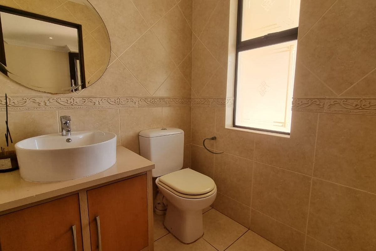 A well-maintained guest bathroom featuring a modern vessel sink on a vanity cabinet, tiled walls, and a window for natural light.