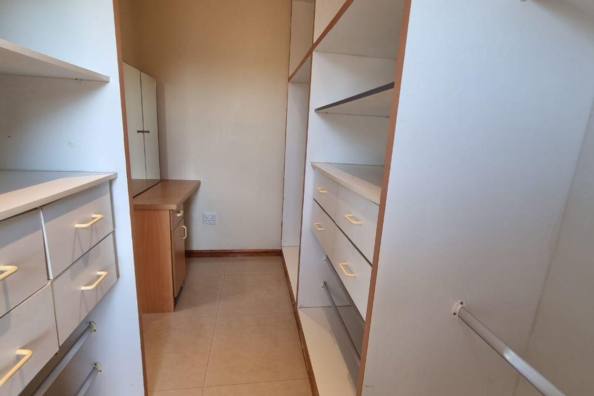A walk-in dressing area featuring built-in cabinetry, hanging rails, and a vanity station with tiled flooring.