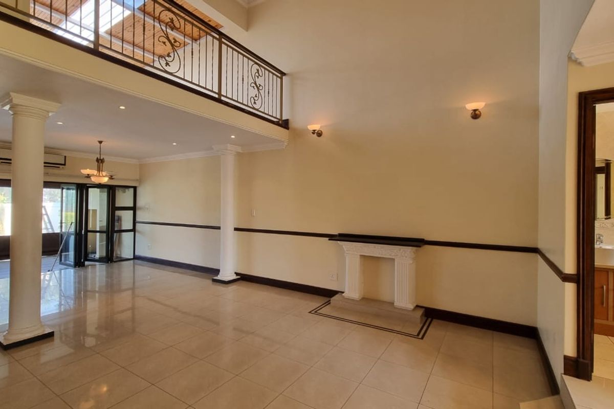 Spacious double-volume living area featuring a decorative fireplace, tiled flooring, and a mezzanine balcony with wrought iron railings, offering an open and airy atmosphere.