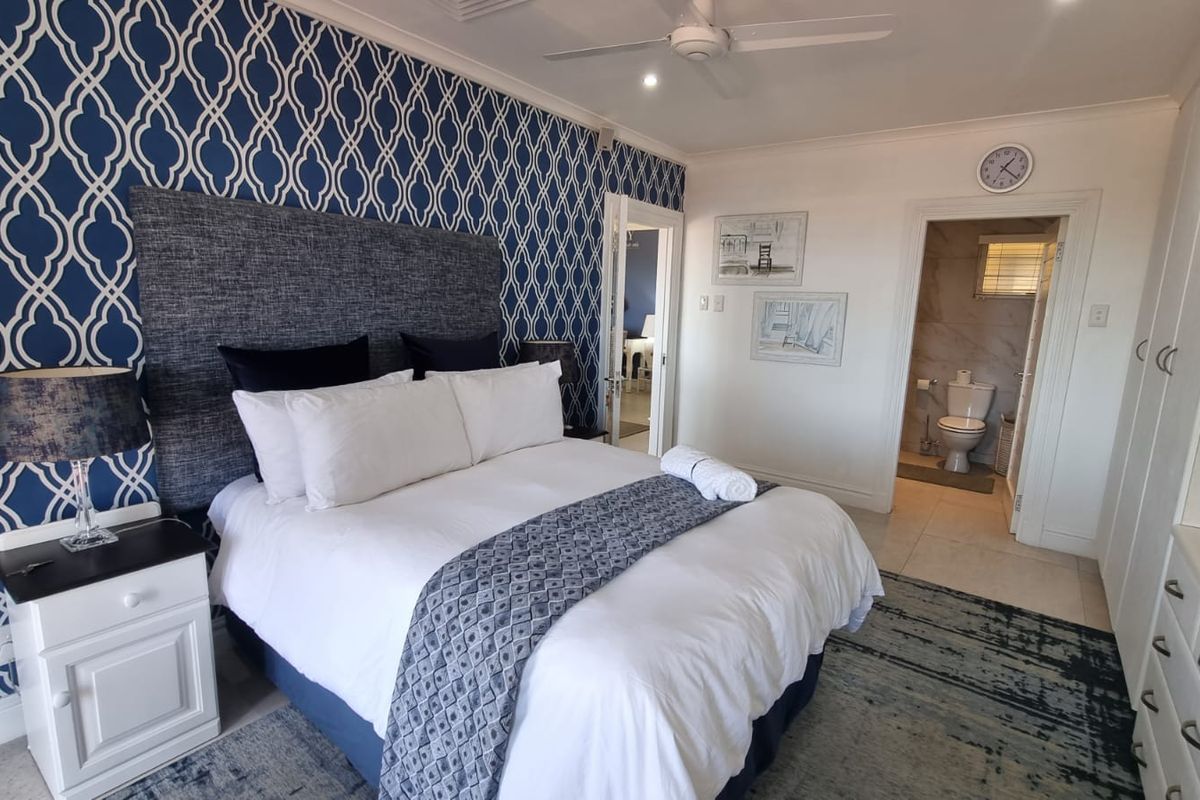 Spacious bedroom featuring a decorative accent wall, ceiling fan, built-in storage, and direct access to an en-suite bathroom with tiled flooring.