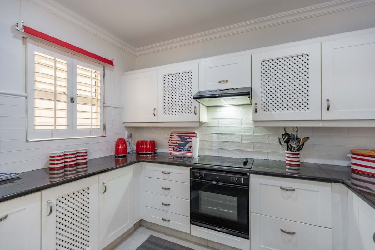 A well-maintained kitchen featuring white cabinetry, dark granite countertops, integrated oven and hob, and classic plantation shutters.