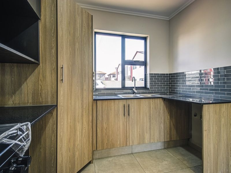 Modern kitchen featuring wood-look cabinetry, granite countertops, and a stylish subway tile backsplash with a stainless steel sink.
